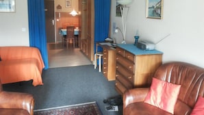 A room with two beds, a desk with a lamp, a chair, a dresser, and a dining area in the background. - Golfpark B 14 Appartement/Fewo, Dusche oder Bad, WC 1½-Zimmerwohnung by Interhome (Davos)