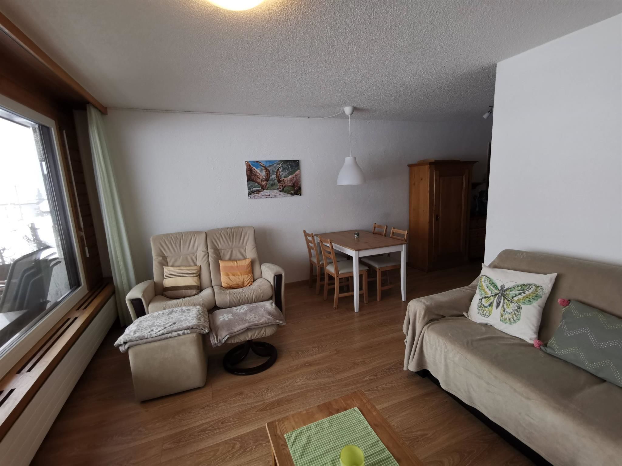 A living room with a sofa, armchair, ottoman, dining table, chairs, and a window.