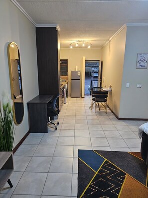 A modern interior with a kitchen, dining area, and a hallway leading to a door. - Stylish Studio Apartment In Fourways (Sandton)