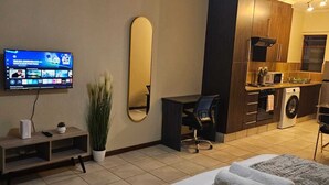 A hotel room with a bed, a desk, a TV, a mirror, and a kitchenette. - Stylish Studio Apartment In Fourways (Sandton)