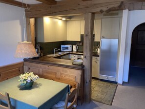 A kitchen with wooden cabinetry, a microwave, a sink, and a dining area with a table and chairs. - Albeina Hus Appartement/Fewo, Dusche oder Bad, WC 2-Zimmerwohnung by Interhome (Klosters)