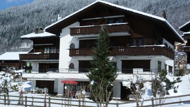 A multi-story building with balconies, a covered outdoor seating area, and a snowy mountain backdrop. - Albeina Hus Appartement/Fewo, Dusche oder Bad, WC 2-Zimmerwohnung by Interhome (Klosters)