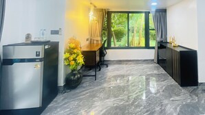 Una cocina moderna con refrigerador, un área de comedor con mesa y sillas, una ventana con vista a follaje, y un reloj decorativo en la pared.