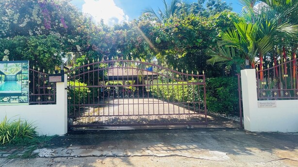 Una entrada con reja a una propiedad, con un cartel que anuncia villas con piscina en alquiler.