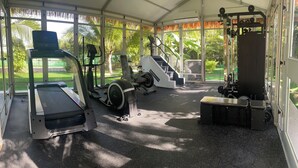 Un gimnasio techado con equipo de ejercicios, ventanas amplias y vistas a zonas verdes.