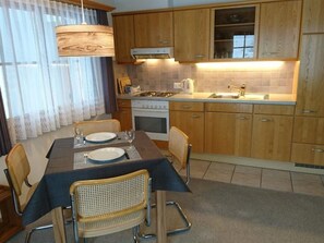 Eine kompakte Küche mit Holzausbau, einem eingebauten Backofen und einem Essbereich mit Tisch für zwei Personen.