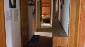 Un couloir étroit avec des portes en bois, un lit au fond et un luminaire au plafond.