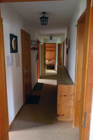 Ein schmaler Flur mit Holztüren, einem Bett am Ende und einer Deckenleuchte.