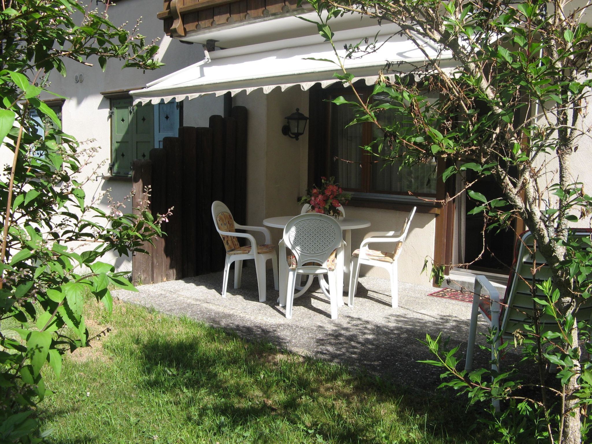 Une terrasse avec une table et des chaises, une clôture en bois et un bâtiment à l’extérieur blanc.