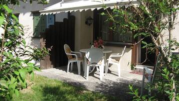 Une terrasse avec une table et des chaises, une clôture en bois et un bâtiment à l’extérieur blanc.