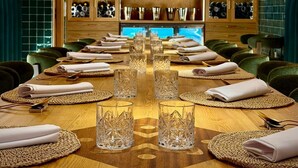 A restaurant with a long wooden table set for a meal, surrounded by green upholstered chairs.