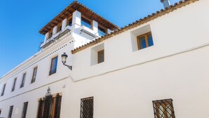 A white building with a tiled roof, multiple windows, and a balcony with a wooden railing.
