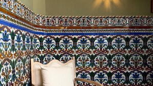 A room with a patterned tile wall, a wooden chair, and a round wooden table.