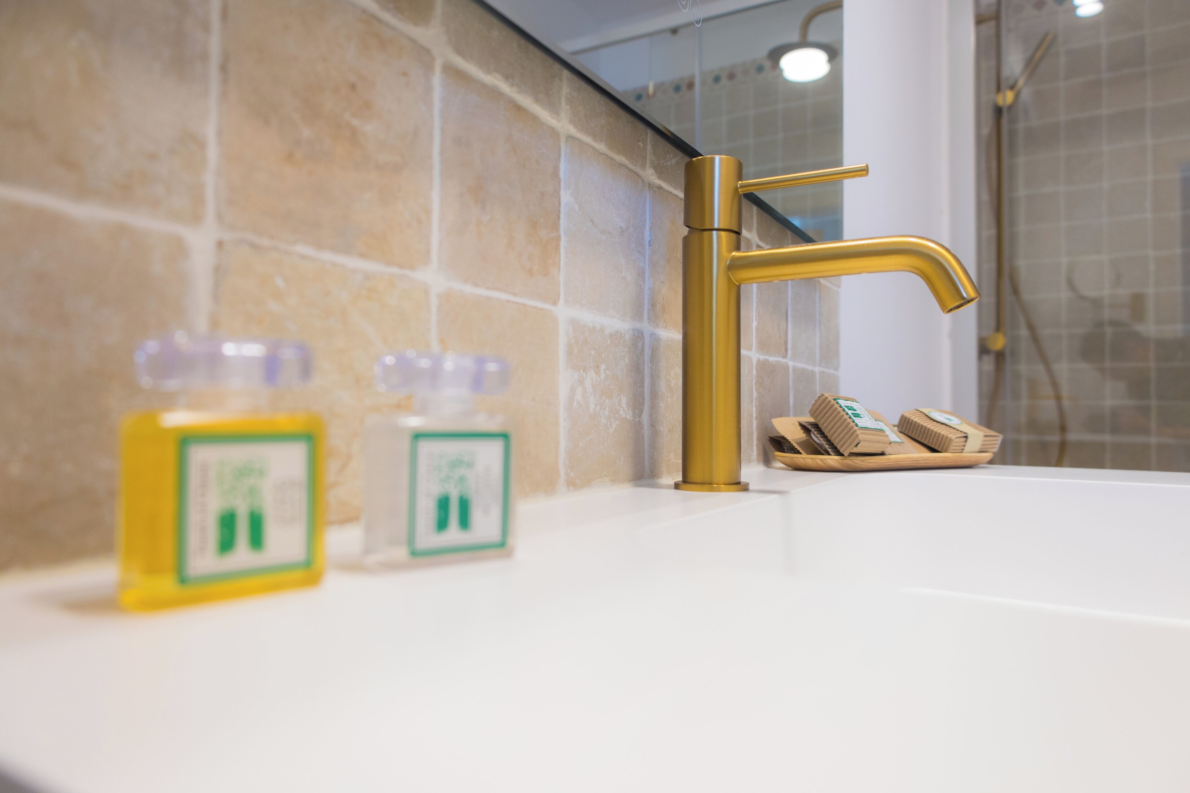 A bathroom with a gold faucet, beige tiles, and two soap dispensers on the counter.