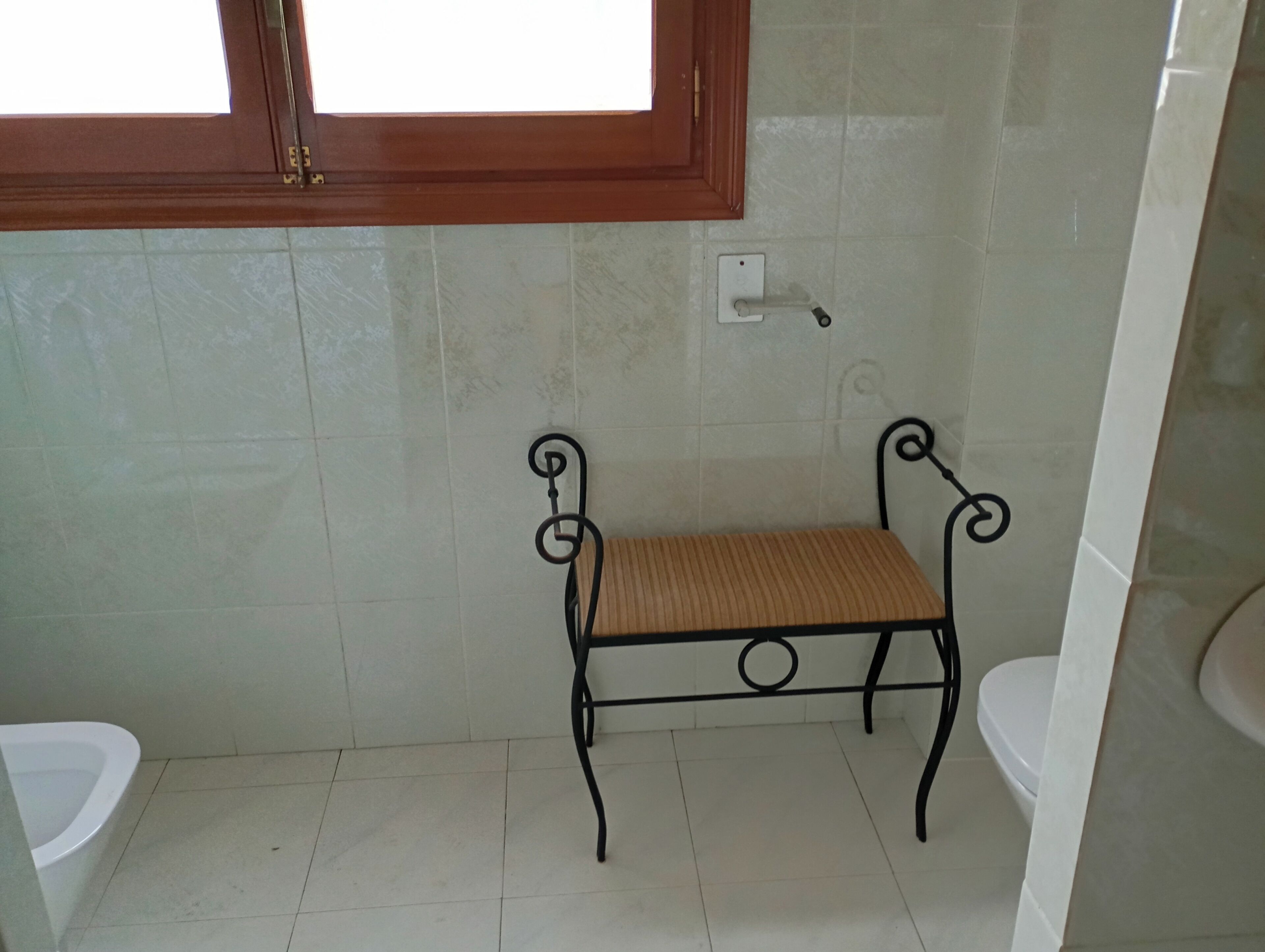 A bathroom with a bench, a toilet, and a window.