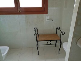 A bathroom with a bench, a toilet, and a window.