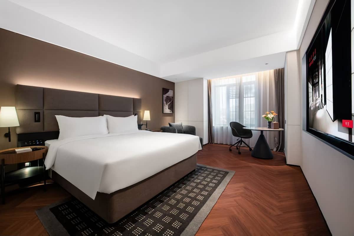 A hotel room with a large bed, bedside tables, a desk, a chair, and a TV.