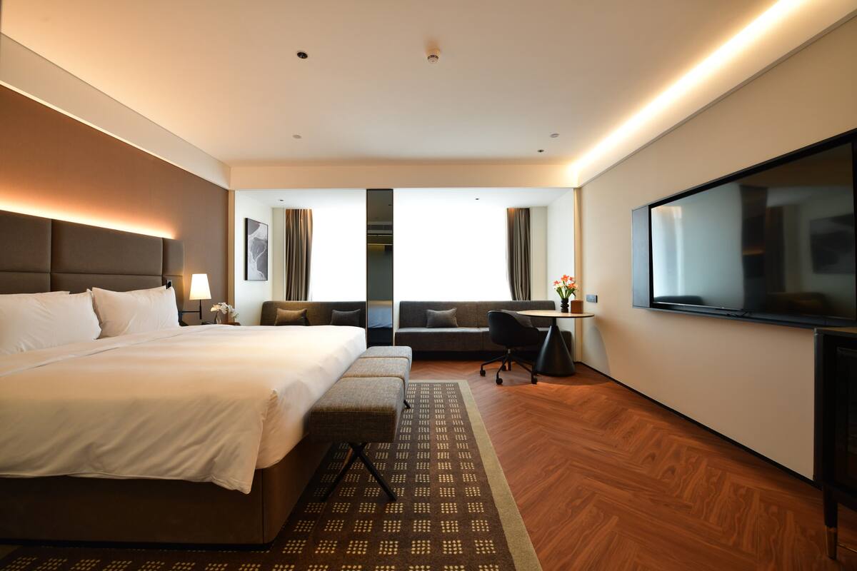 A hotel room with a large bed, a desk, a sofa, and a TV.