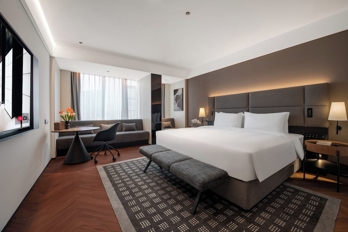 A modern hotel room with a large bed, a desk, a sofa, and a view of the city.