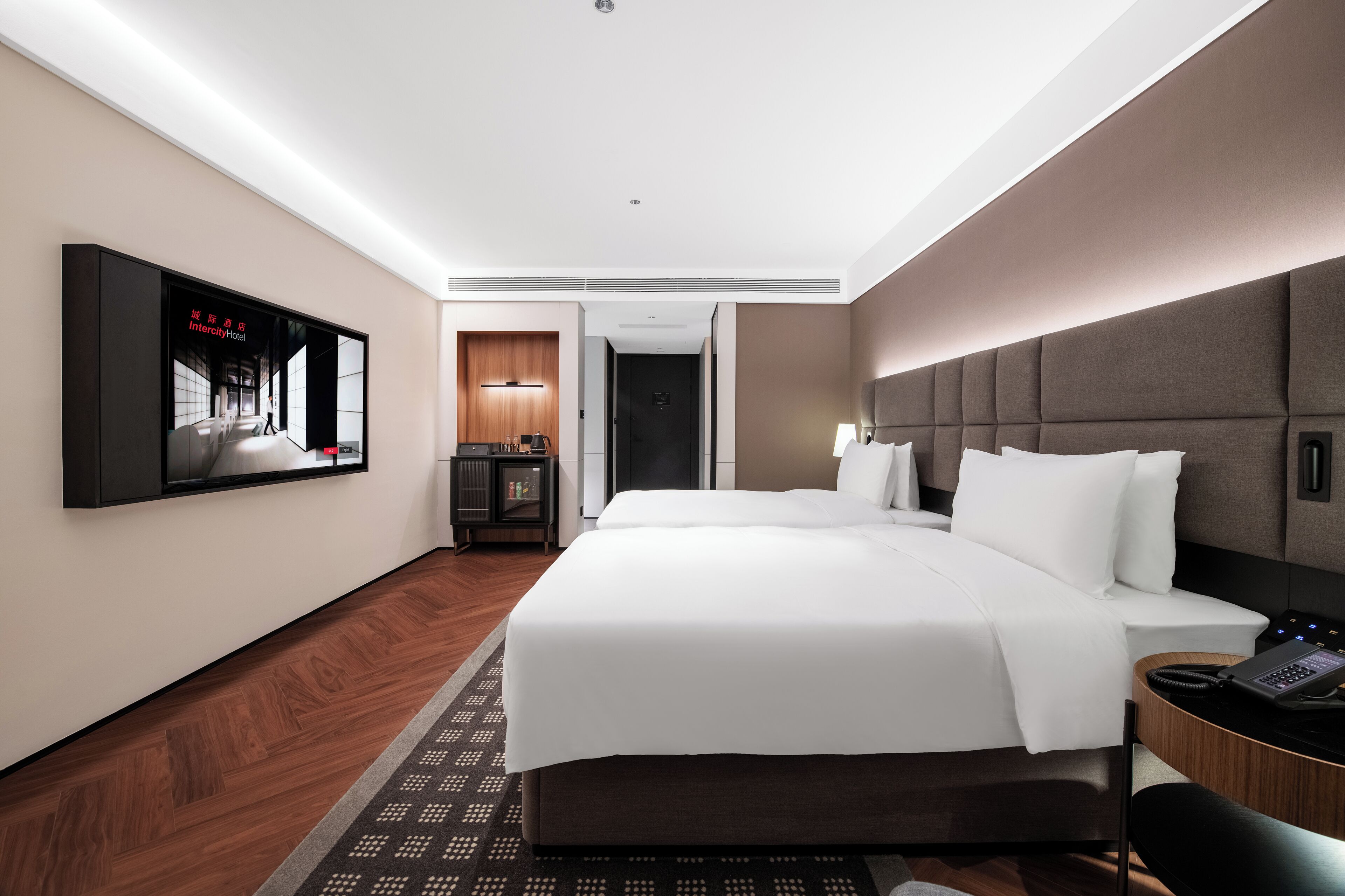 A hotel room with a large bed, a desk with a phone, a TV mounted on the wall, and a door leading to another room.