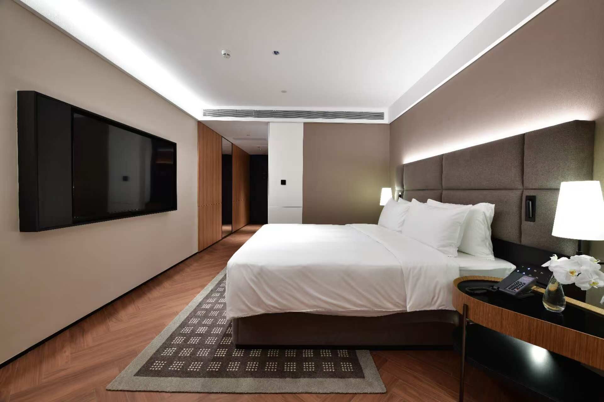 A hotel room with a bed, a desk with a phone, a TV, and a lamp.