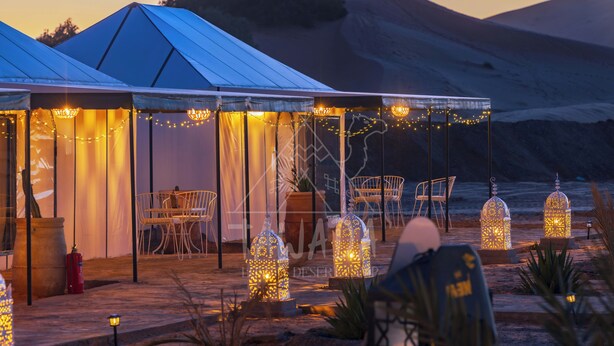 A tented outdoor area with tables and chairs, string lights, and lanterns. - TAWADA LUXURY DESERT CAMP (Merzouga)