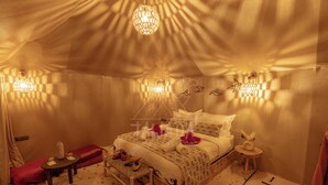 A tent-style room with a bed, bedside tables, and decorative wall lights. - TAWADA LUXURY DESERT CAMP (Merzouga)