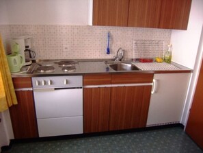 A kitchen with a stove, sink, and wooden cabinets.