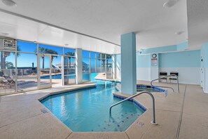 Una piscina interior con paredes de vidrio transparente, suelo de baldosas y una silla para socorrista.