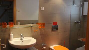 Un bagno moderno con ripiano in vetro, lavandino bianco, WC arancione e zona doccia.