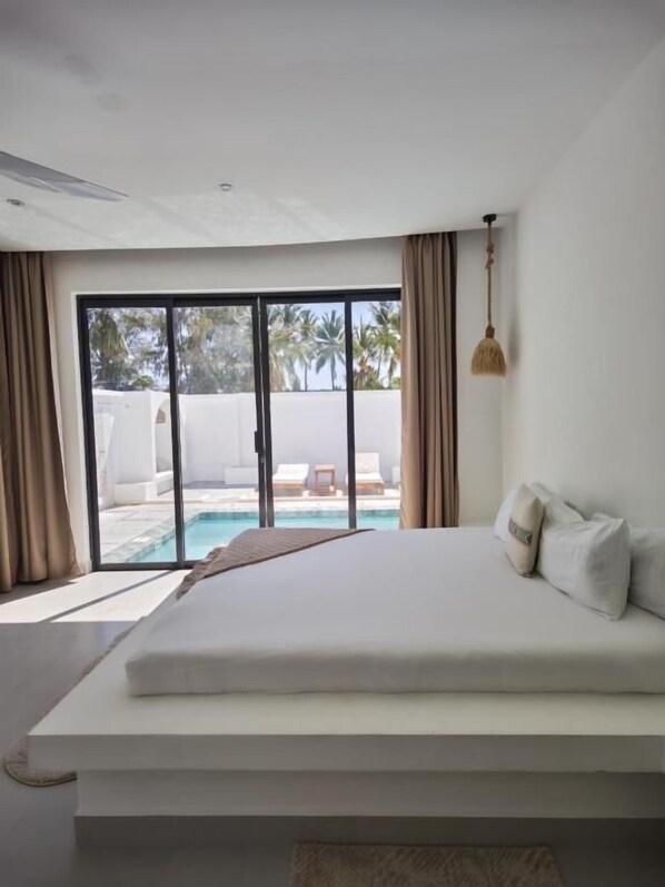 Une chambre moderne avec un grand lit, une vue sur une piscine et une porte-fenêtre coulissante.