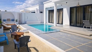 A modern outdoor pool area with lounge chairs, a table, and a covered seating area.