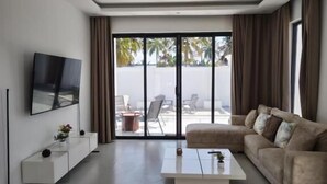 A modern living room with a flat-screen TV, a sofa, a coffee table, and a ceiling fan.