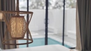 A bedroom with a bed, a hanging light fixture, and a view of a swimming pool.