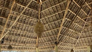 A restaurant with a thatched roof, wooden tables and chairs, and a view of the beach.