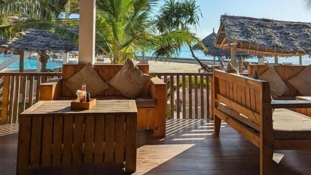 A wooden deck with seating, a thatched roof, and a view of a pool and palm trees.