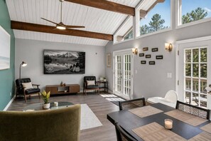 A spacious living room with a high ceiling, large windows, a fireplace, and a dining area. - Sleeps 12 • Hot Tub • 5 Min to Lake Beach (Long Pond)