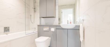 A modern bathroom with a glass-enclosed shower, a white toilet, and a grey vanity with a sink.