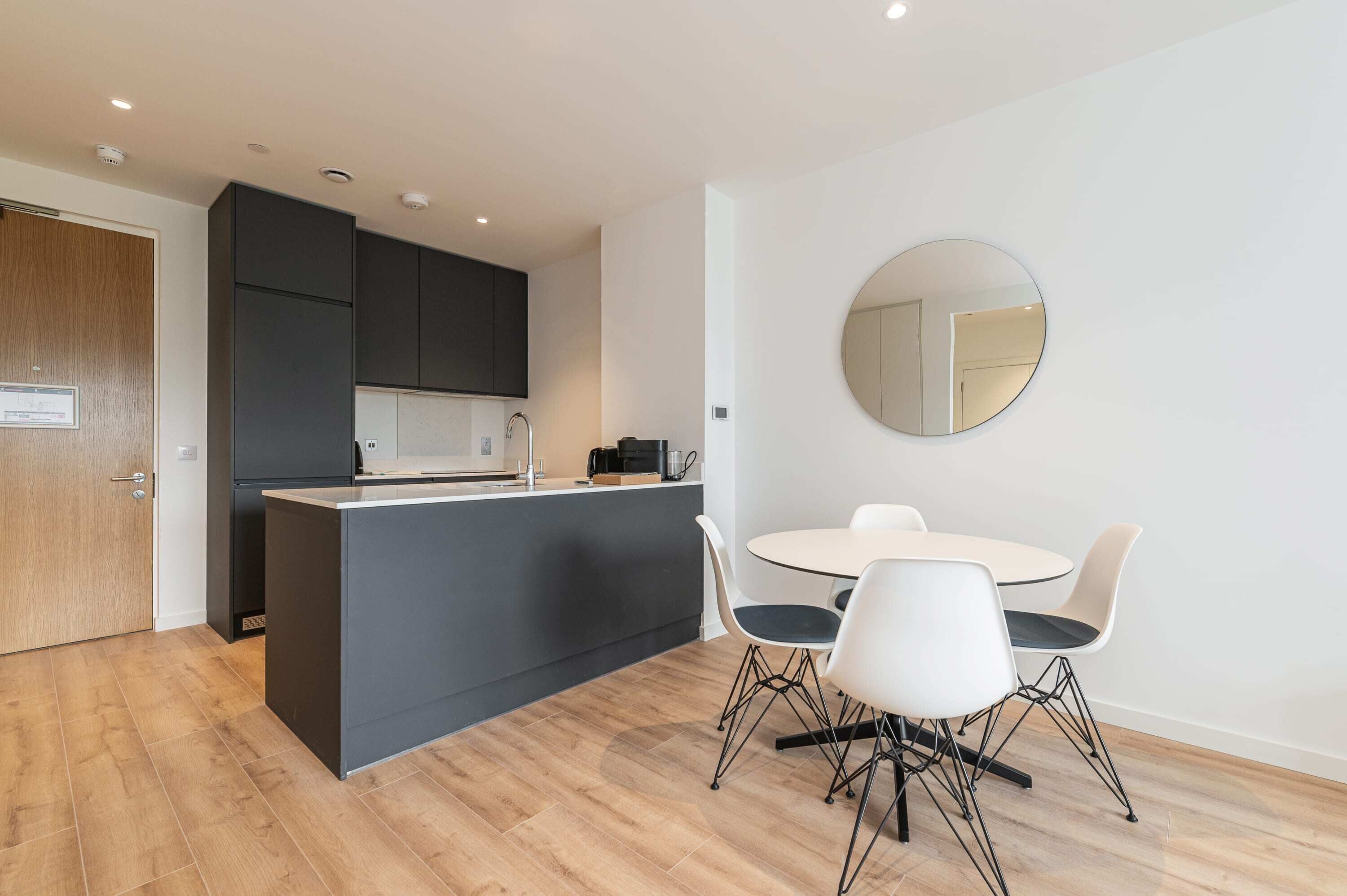 Una cocina moderna con una isla central, una mesa de comedor blanca con sillas y un espejo redondo en la pared.