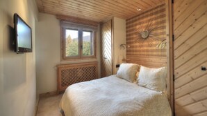 Une chambre à coucher avec un lit, une télévision, une fenêtre et un plafond en bois.