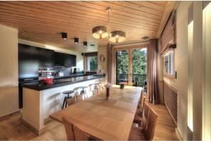 A modern kitchen with a central island, bar stools, and a dining table. - Luxurious family apartment - Megève Centre - Iconic archi Henry Jacques LeMême (Megève)