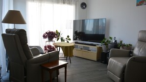 Ein Wohnzimmer mit einer Couch, einem Tisch, einem Fernseher und einer Pflanze.