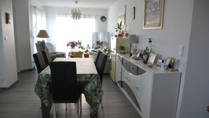 Ein Essbereich mit einem für sechs Personen gedeckten Tisch, umgeben von Stühlen, einer Couch und einem Fernseher.