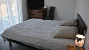 Ein Schlafzimmer mit einem großen Bett, einem Fernseher auf einer Kommode, einem Sessel und einer Lampe.