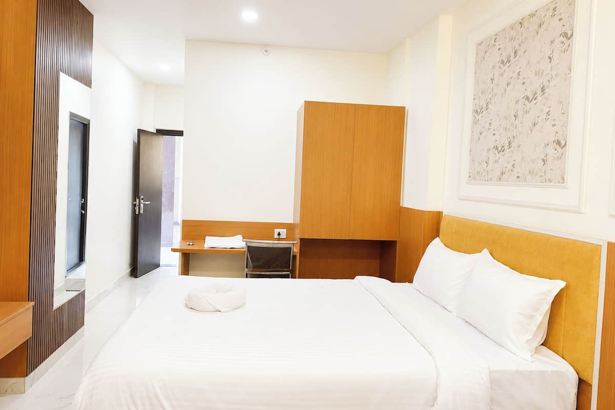 A hotel room with a bed, a desk, a wardrobe, and a painting on the wall.