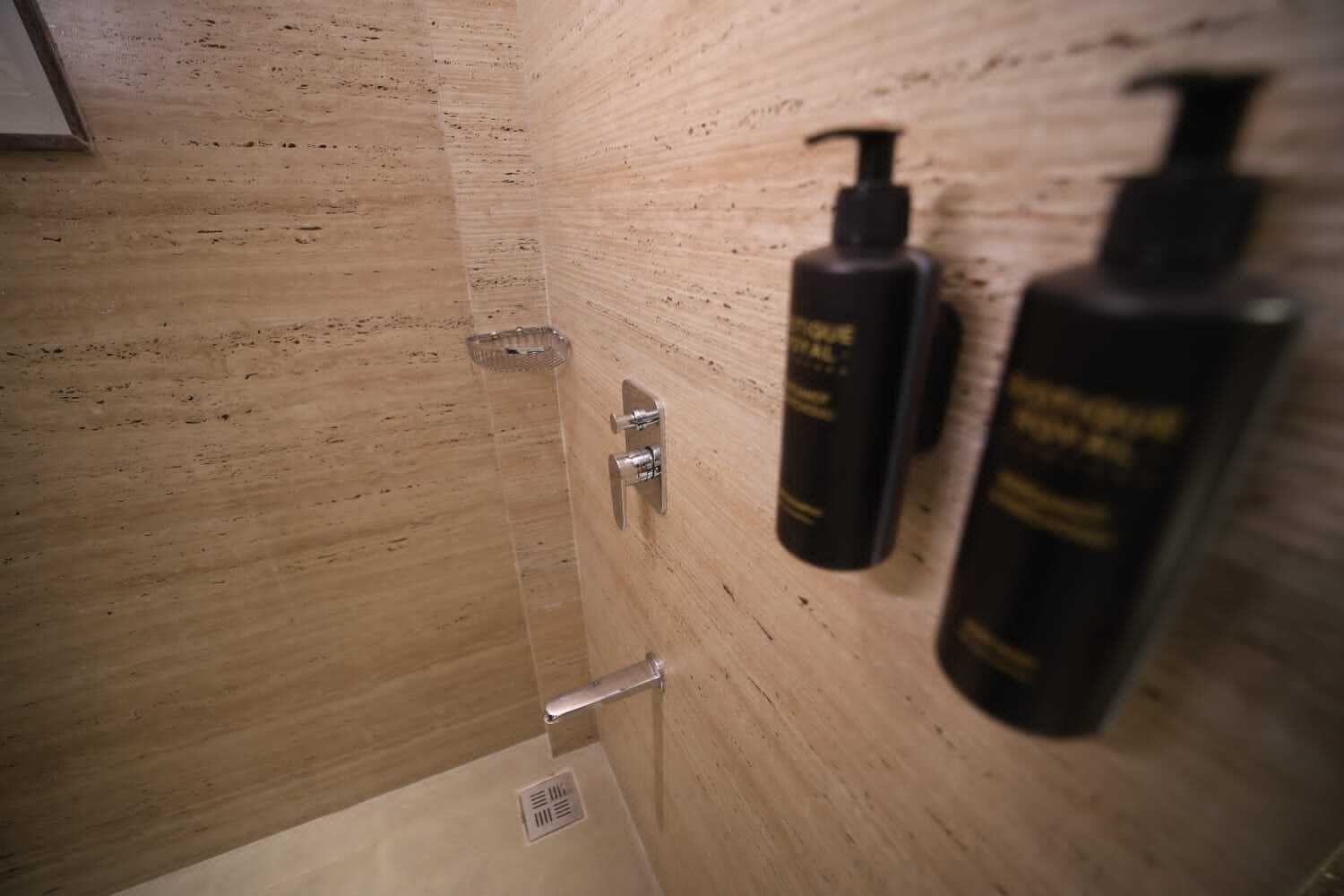 A wooden shower enclosure with a glass door, a showerhead, and two black bottles on the wall.