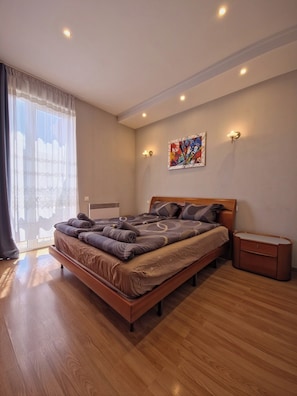Un dormitorio moderno con una cama grande, mesitas de noche, una ventana con cortinas y un cuadro abstracto de colores en la pared.