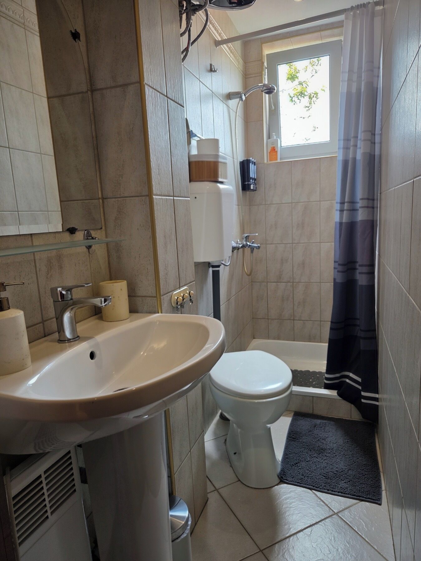 Une salle de bain équipée d’un lavabo, de toilettes, d’une douche et d’une fenêtre donnant sur les arbres.