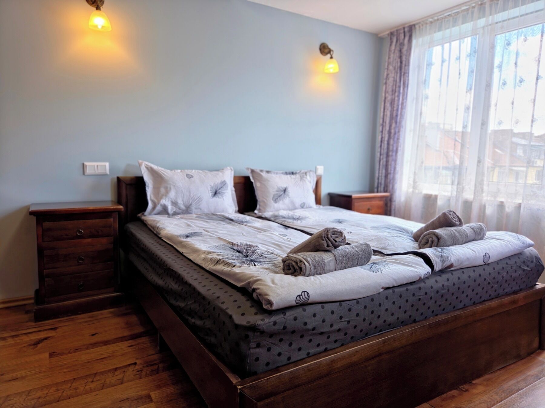 Een slaapkamer met een houten bed, twee nachtkastjes, een venster met gordijnen.