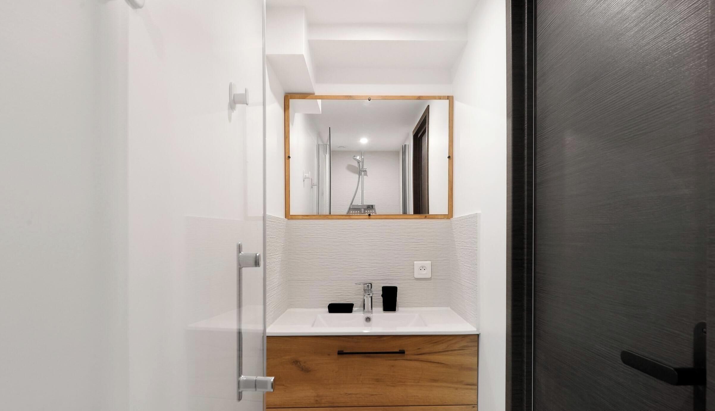 A modern bathroom with a white vanity, a wooden cabinet, a mirror, and a shower.